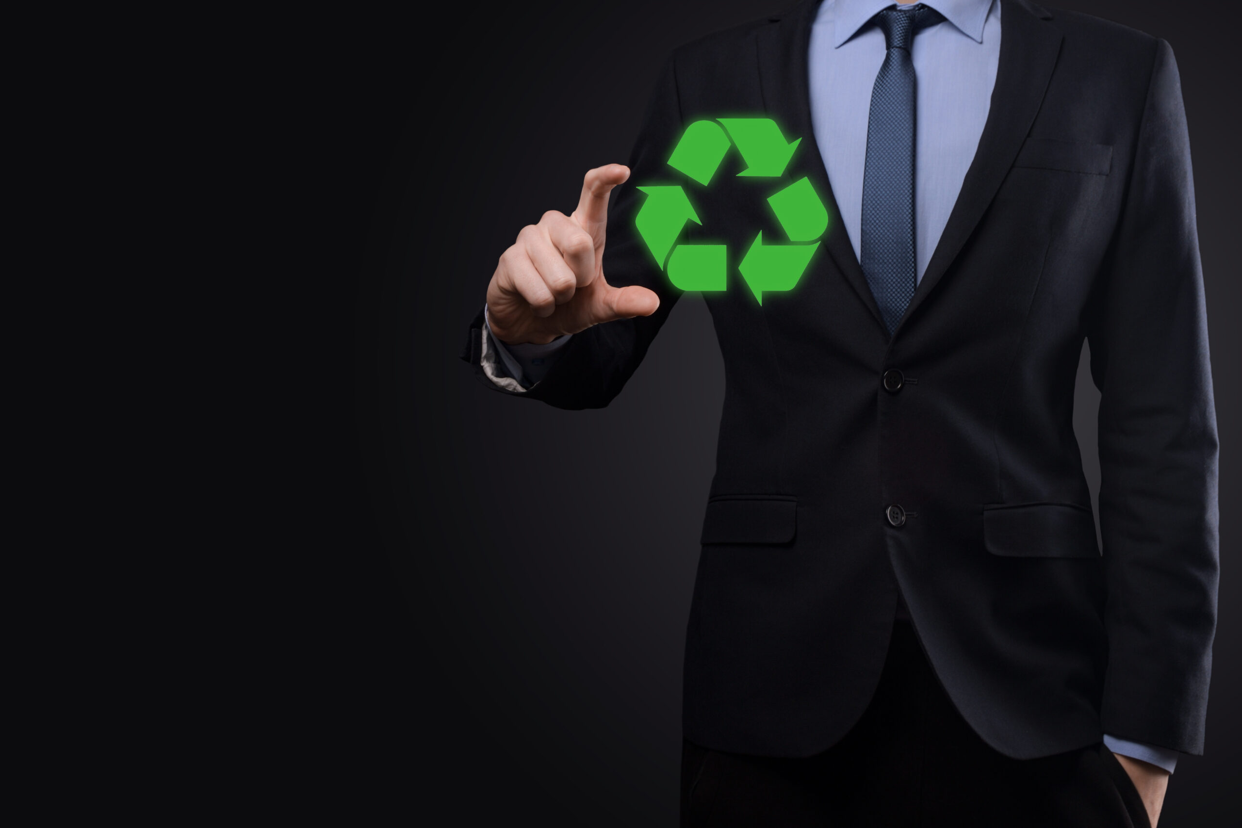 Businessman in suit over dark background holds an recycling icon, sign in his hands. Ecology, environment and conservation concept. Neon red blue light.